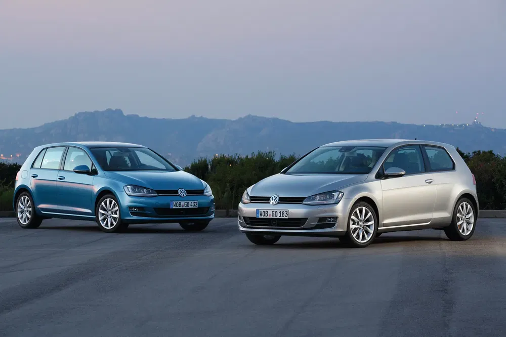 Deux Volkswagen Golf stationnées sur une route avec un arrière-plan montagneux au crépuscule.